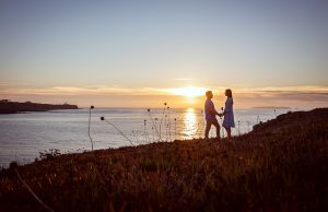 Casal de frente um para o outro durante sessão de namoro ao por do sol à beira mar